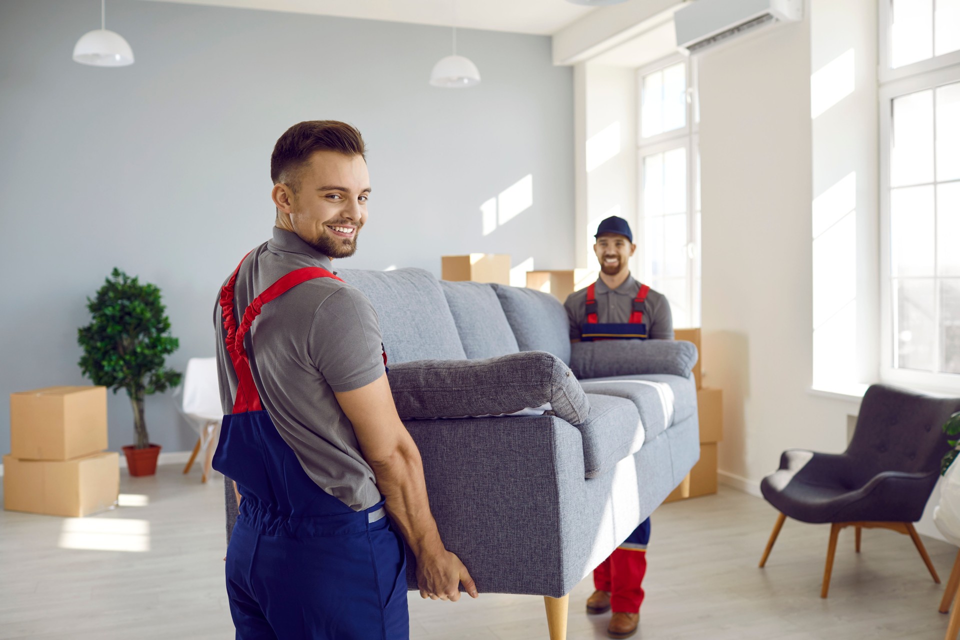 Male workers of furniture delivery service move sofa to customer's new apartment.